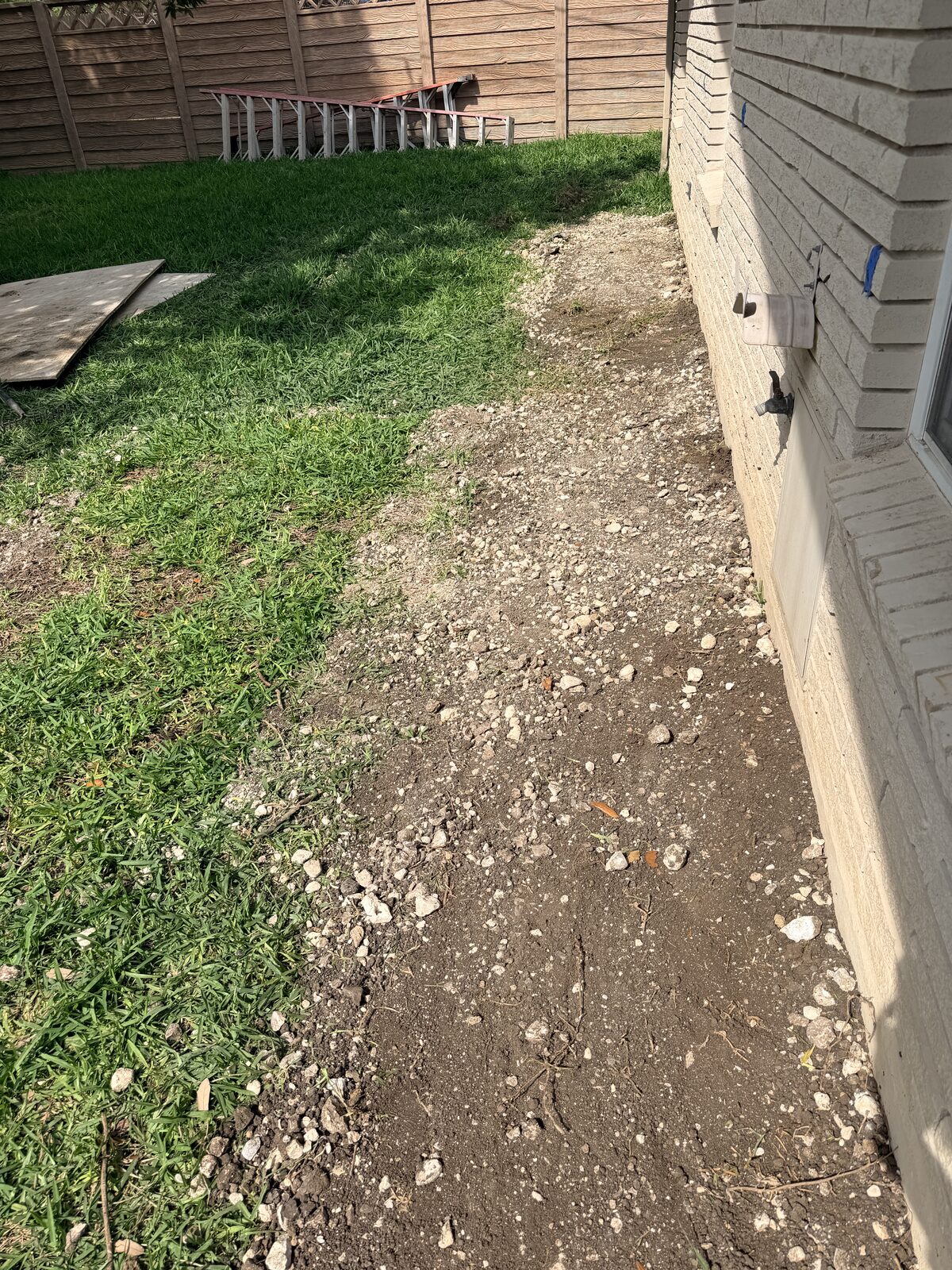 A backfilled access trench along a building wall, restored after the repair.
