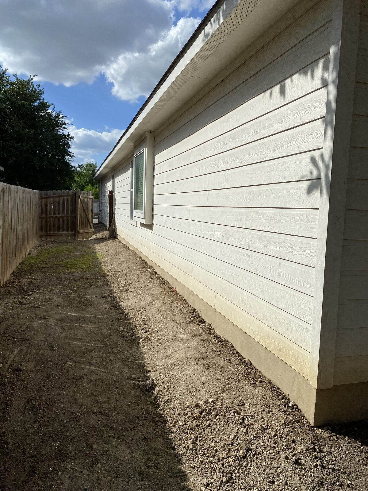 Side yard regraded and backfilled along the foundation after pier work, between home and fence