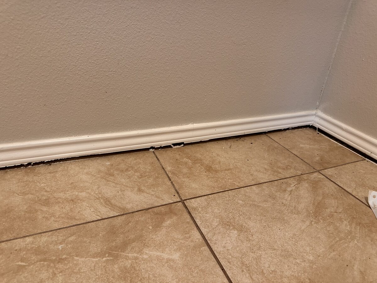 Gap opening beneath a baseboard at a room corner as the slab foundation settles, with caulk pulling apart