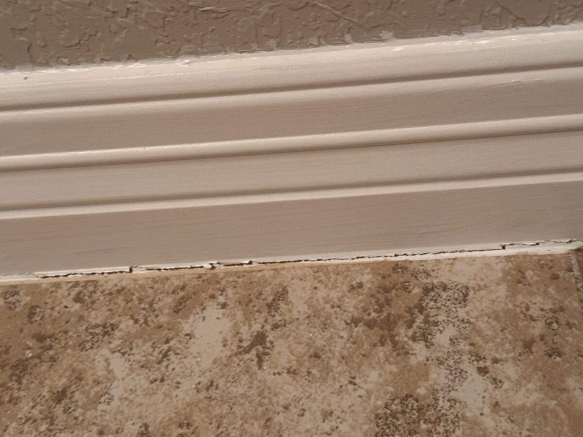 Gap opening beneath baseboard trim along a tile floor, an interior sign of slab settlement