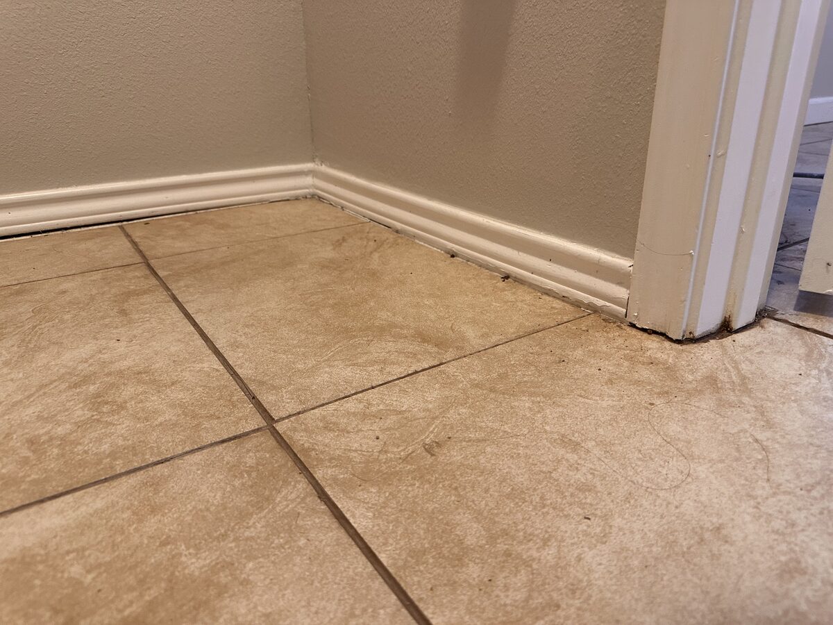 Baseboard lifting away from the tile floor near a doorway, evidence of slab foundation movement