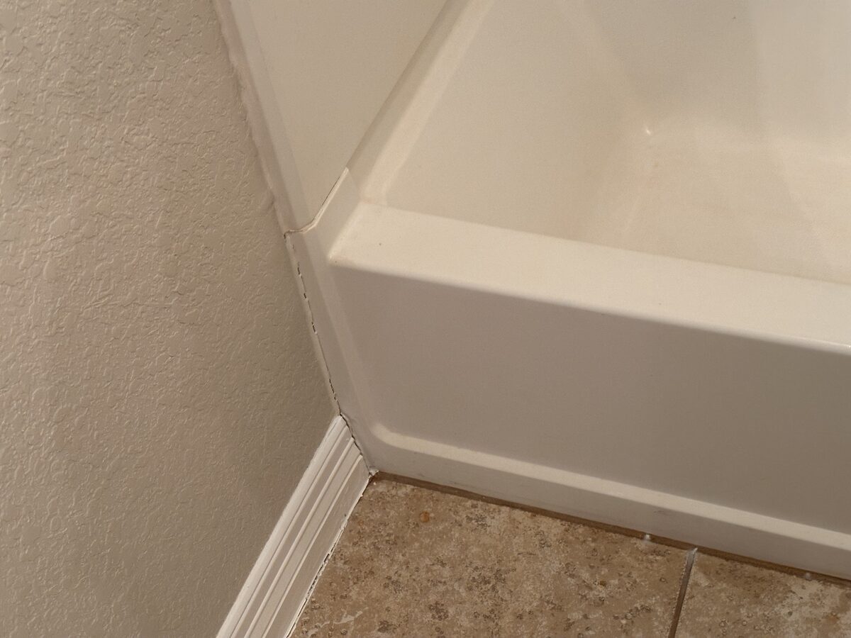 Baseboard separating at a wall corner beside a shower base, caused by foundation movement