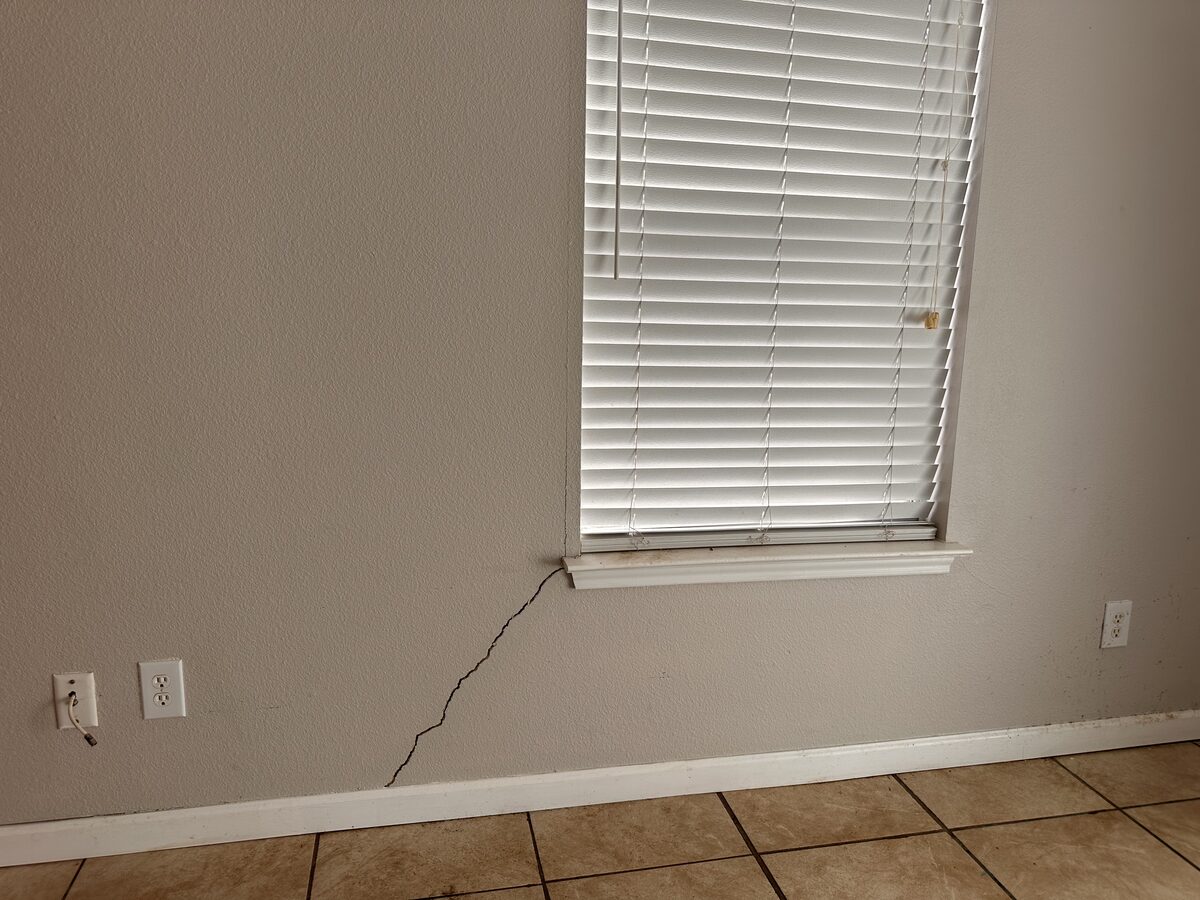 Bedroom wall with a settlement crack running from the window corner down toward an electrical outlet