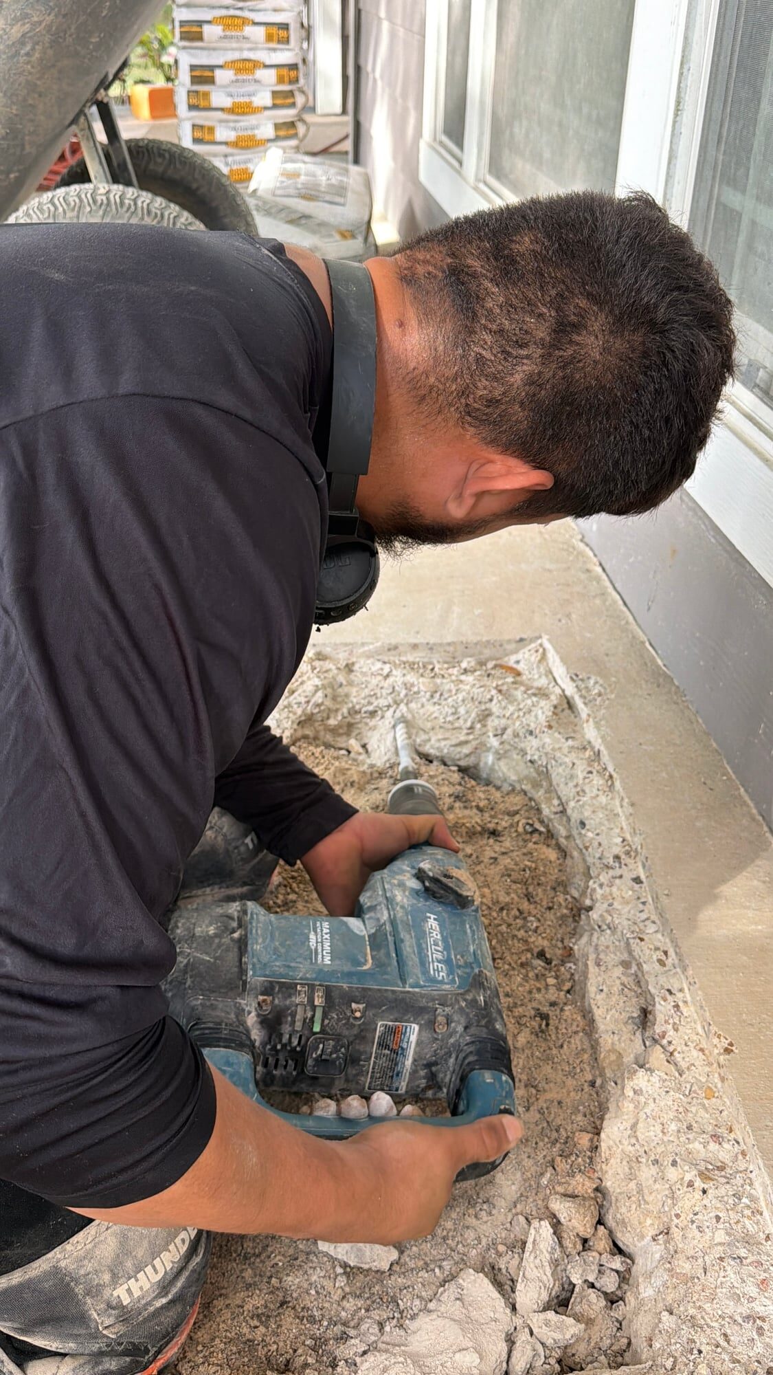 Crew member using a rotary hammer to break out a square section of a covered walkway slab