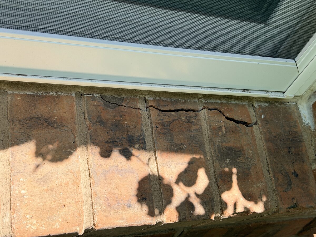 Horizontal crack running through brick and mortar above a window