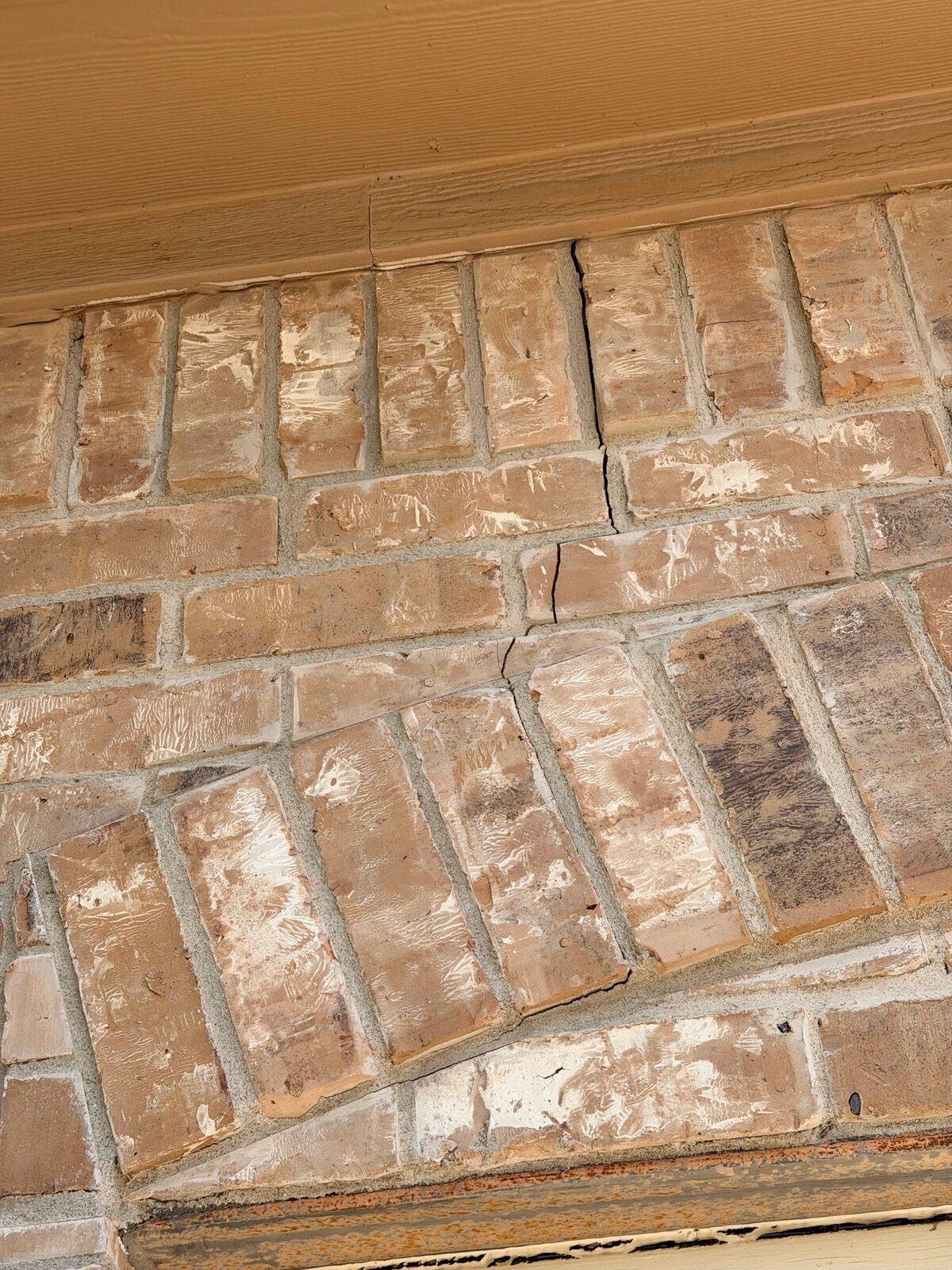Cracked brick and open mortar joints above a window arch with a rusted steel lintel