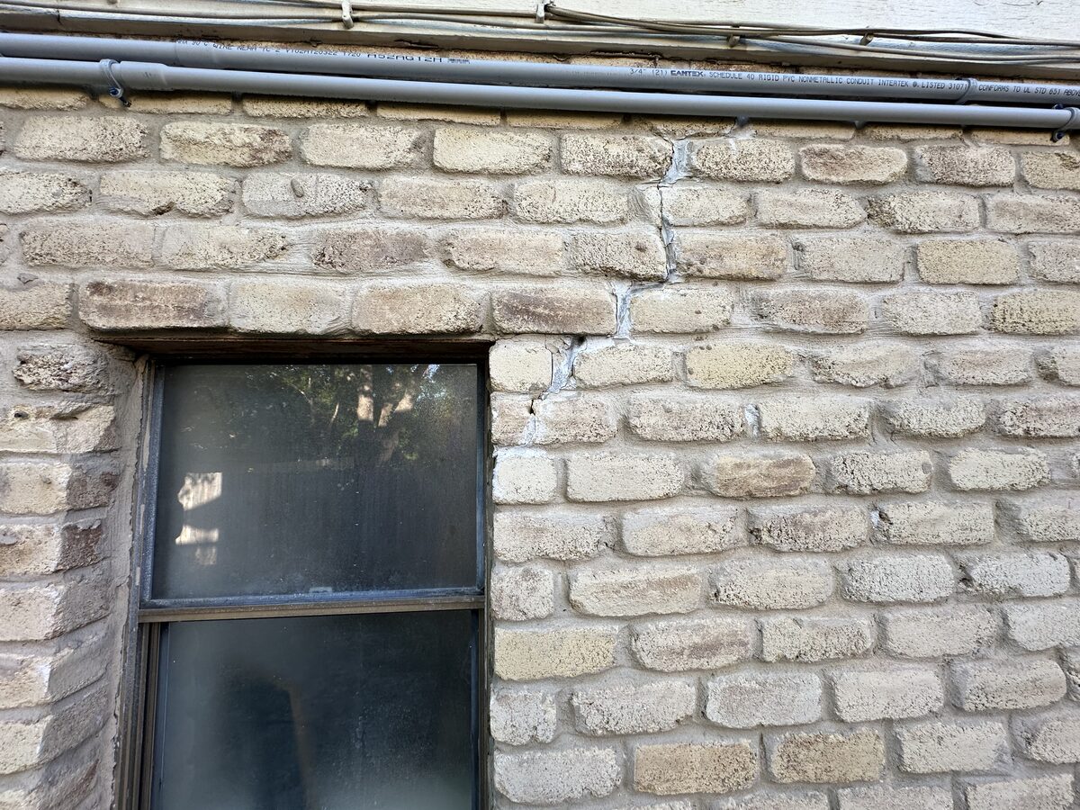 Wide vertical crack in brick veneer next to a steel-framed window, caused by foundation movement