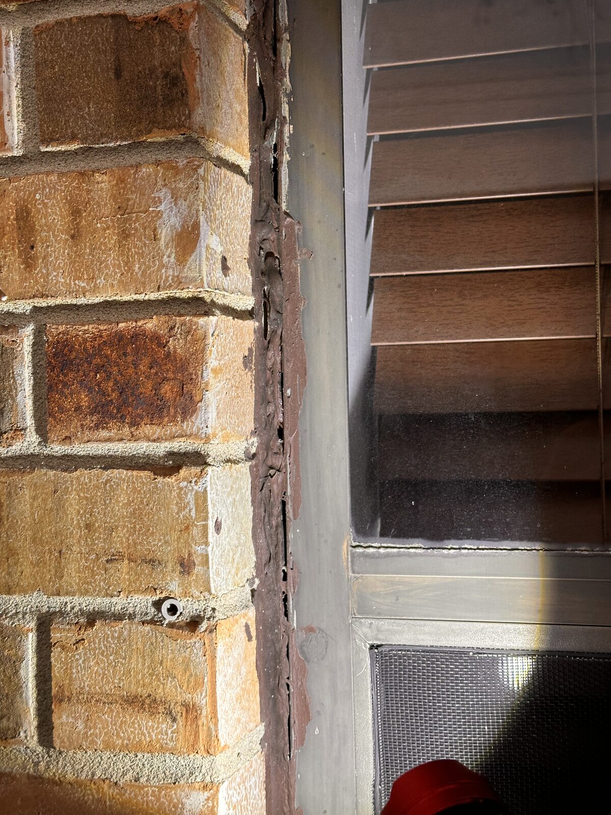 Crack in brick veneer beside window trim at a corner, a common sign of differential foundation settlement
