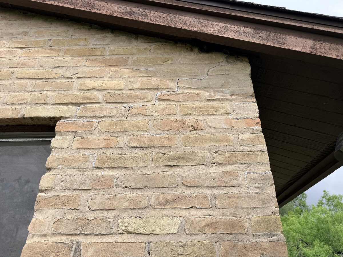Cracked brick at a gable corner just below the roof fascia, exterior evidence of foundation movement