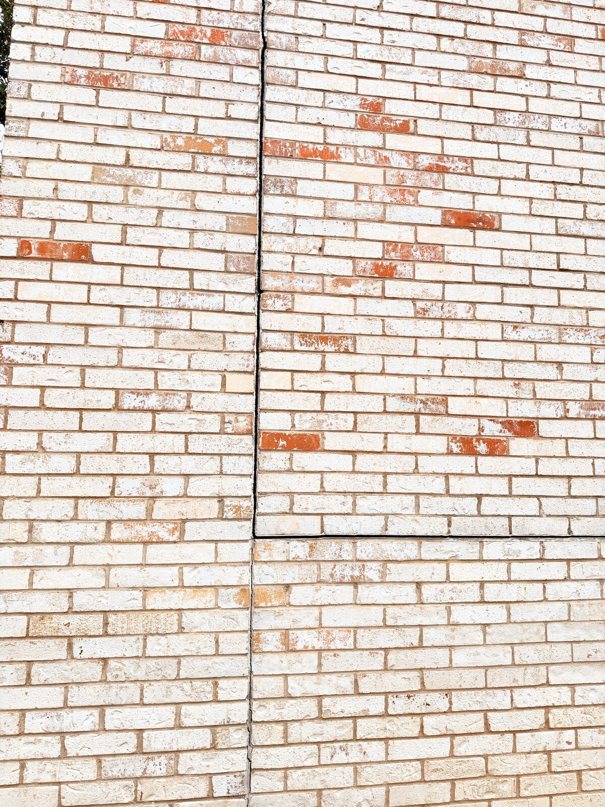Diagonal pattern of replacement bricks beside a repointed joint in a settlement-cracked brick wall
