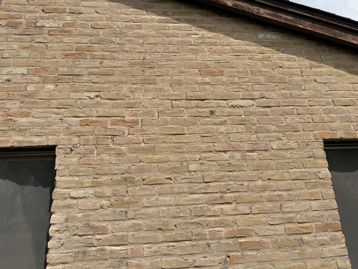 Hairline cracking in the mortar of a brick wall between two windows, an early sign of foundation movement