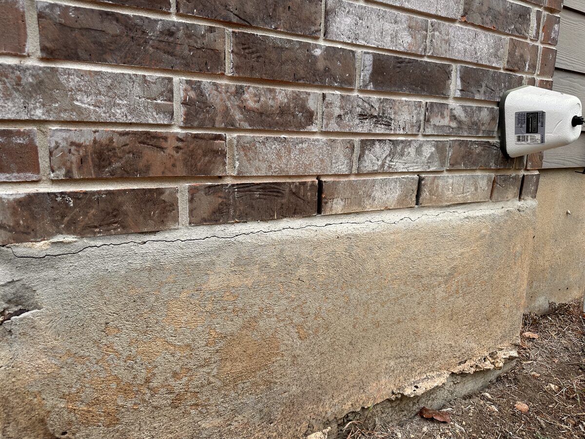 Horizontal crack and efflorescence where brick veneer meets the parged stem wall of a foundation