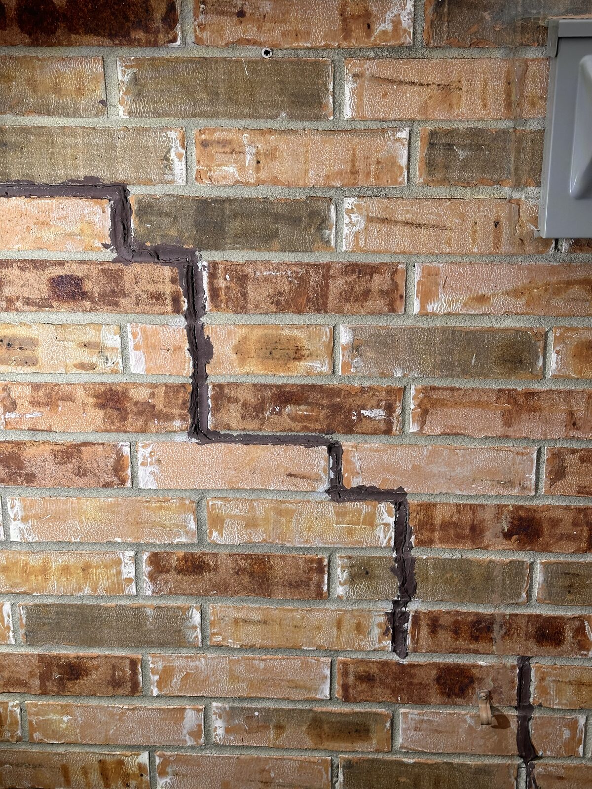 Cracked brick veneer at a wall corner near the utility meter, documented during a foundation inspection
