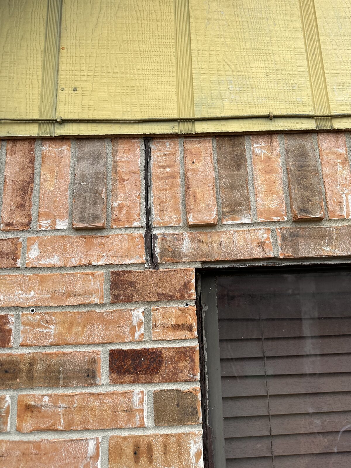 Cracked brick veneer near a vent under lap siding, an exterior symptom of foundation movement