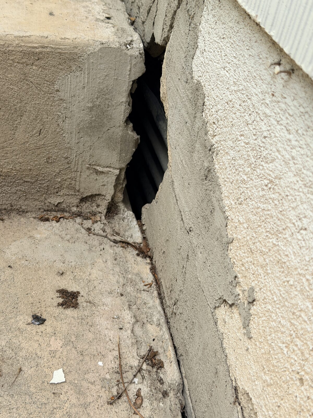 Broken stucco and concrete corner revealing a dark void beneath the beam