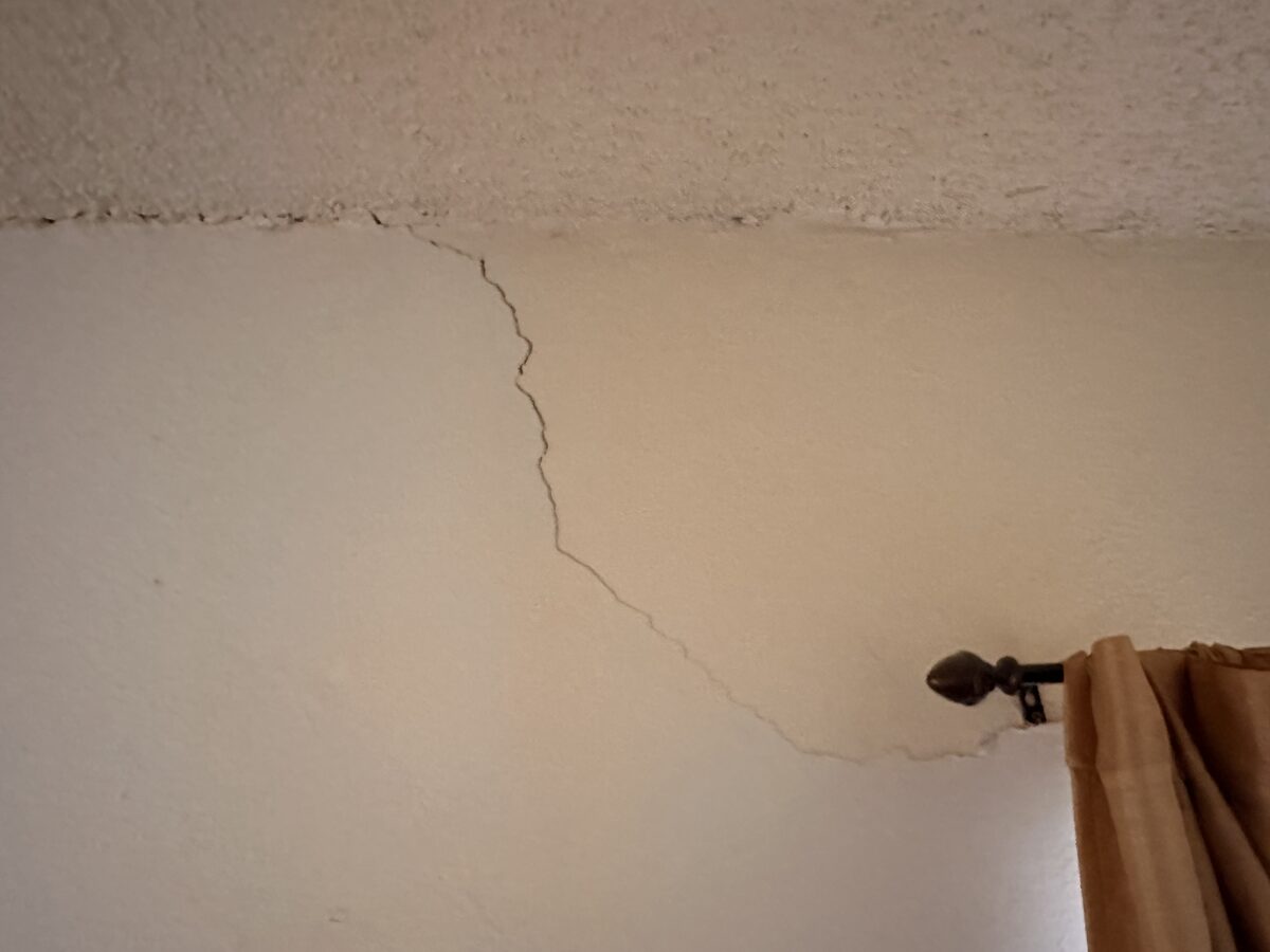 Crack running across the ceiling line above a curtain rod, evidence of foundation settlement