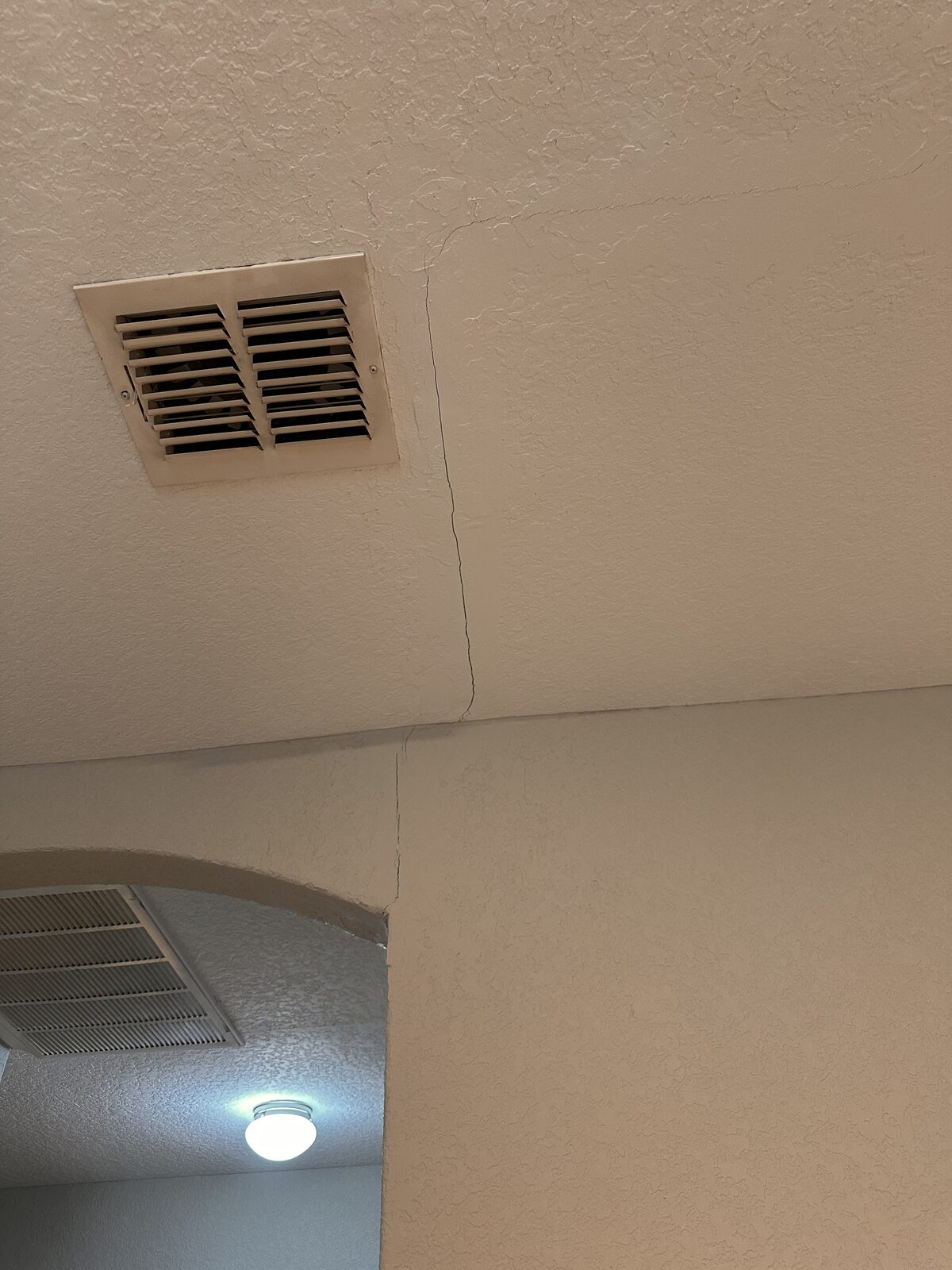 Drywall seam crack in the ceiling beside an air vent above a hallway arch, a foundation settlement sign