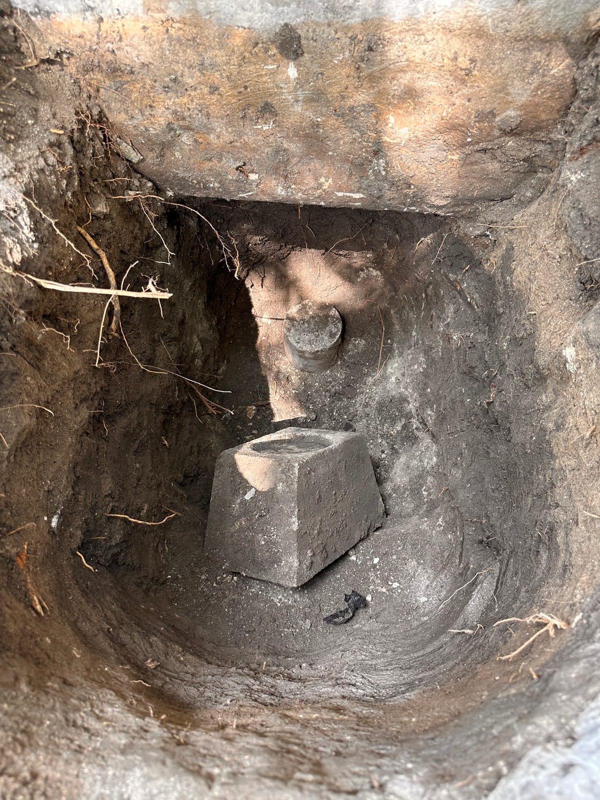 Precast concrete pier section with a steel bracket seated in an excavated pit beside a slab foundation