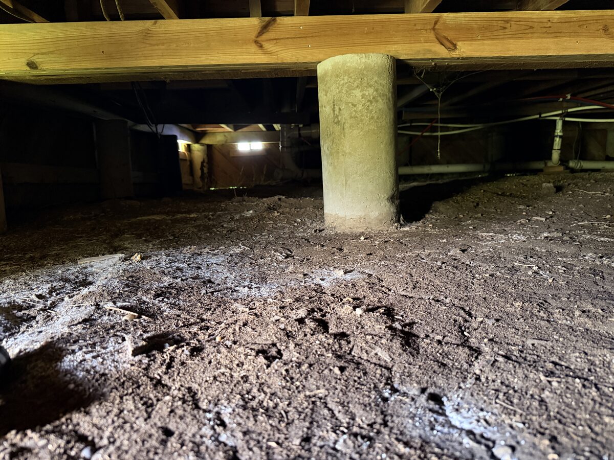 Poured concrete cylinder pier supporting a wood beam in a crawl space