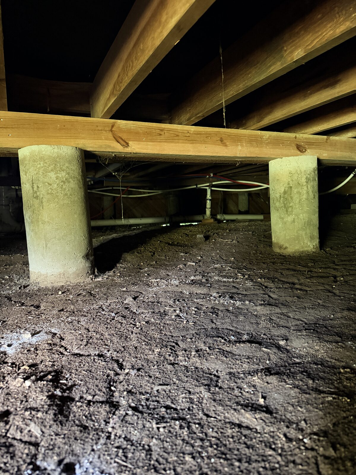 Two concrete cylinder piers supporting a wood beam and floor joists over a dirt crawl space