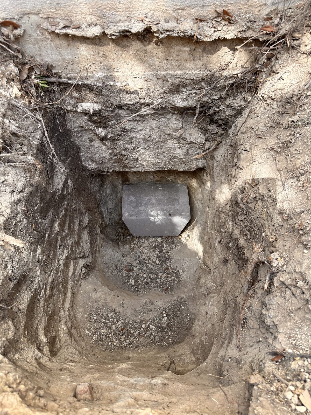 Concrete pile cap seated in an excavated pier pit beneath a home's footing during foundation repair