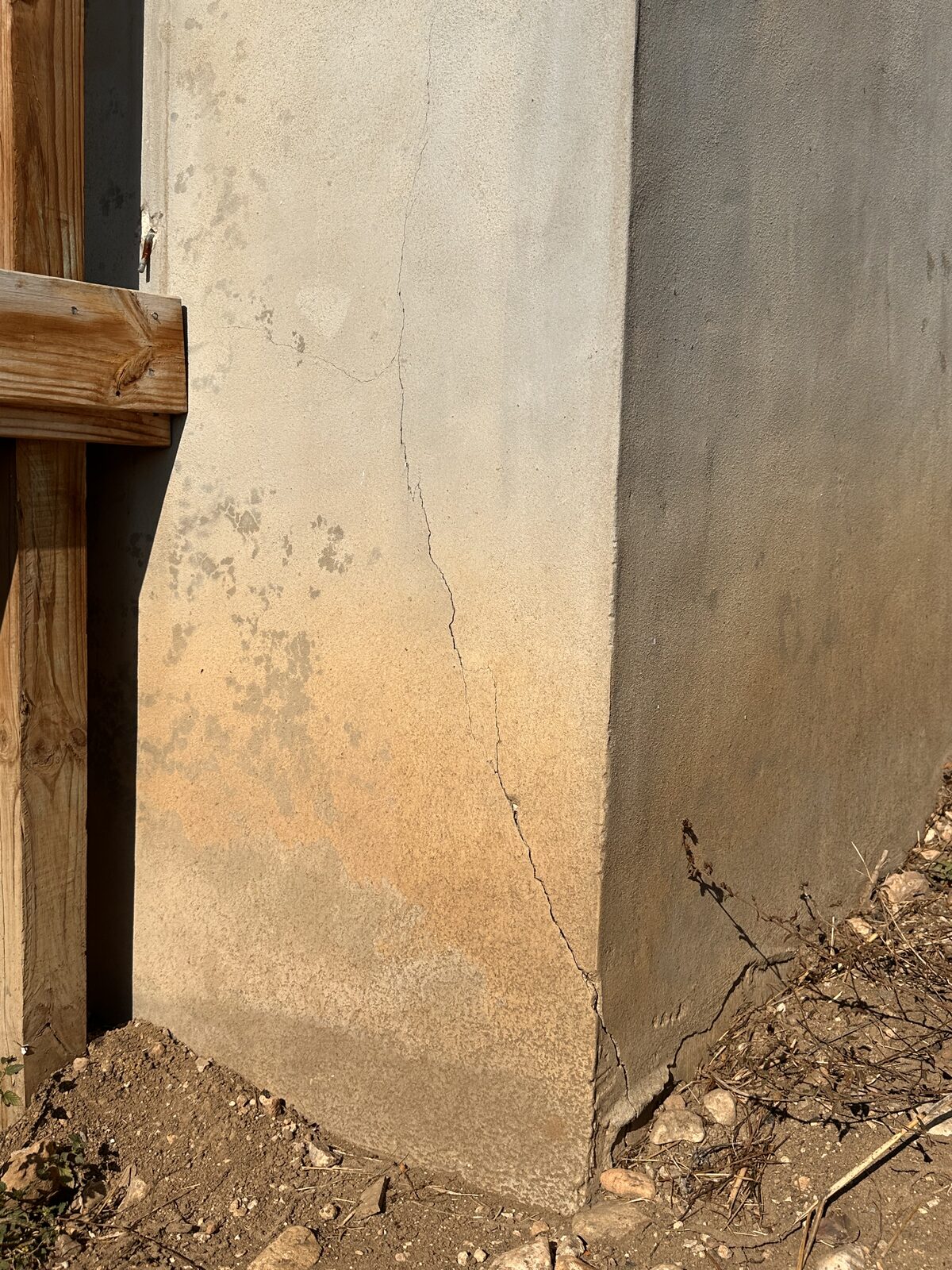 Vertical crack at the corner of a parged foundation wall beside a wooden deck post