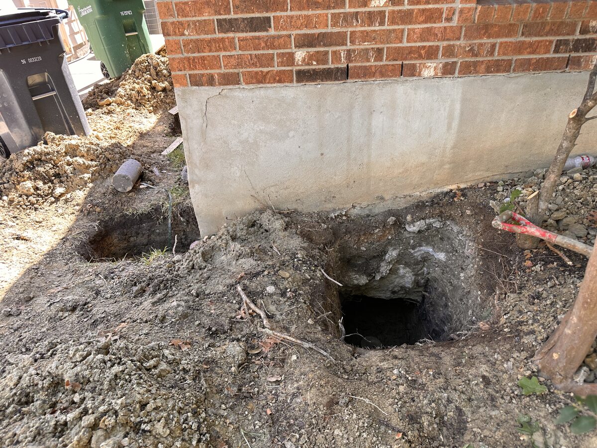 Excavated pier hole at the corner of a brick home exposing the footing and stem wall for repair