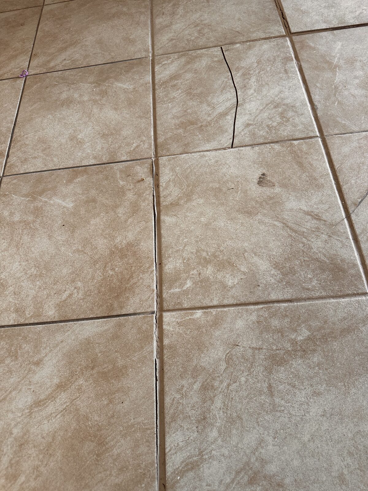 Crack running across ceramic floor tiles, reflecting movement in the concrete slab below