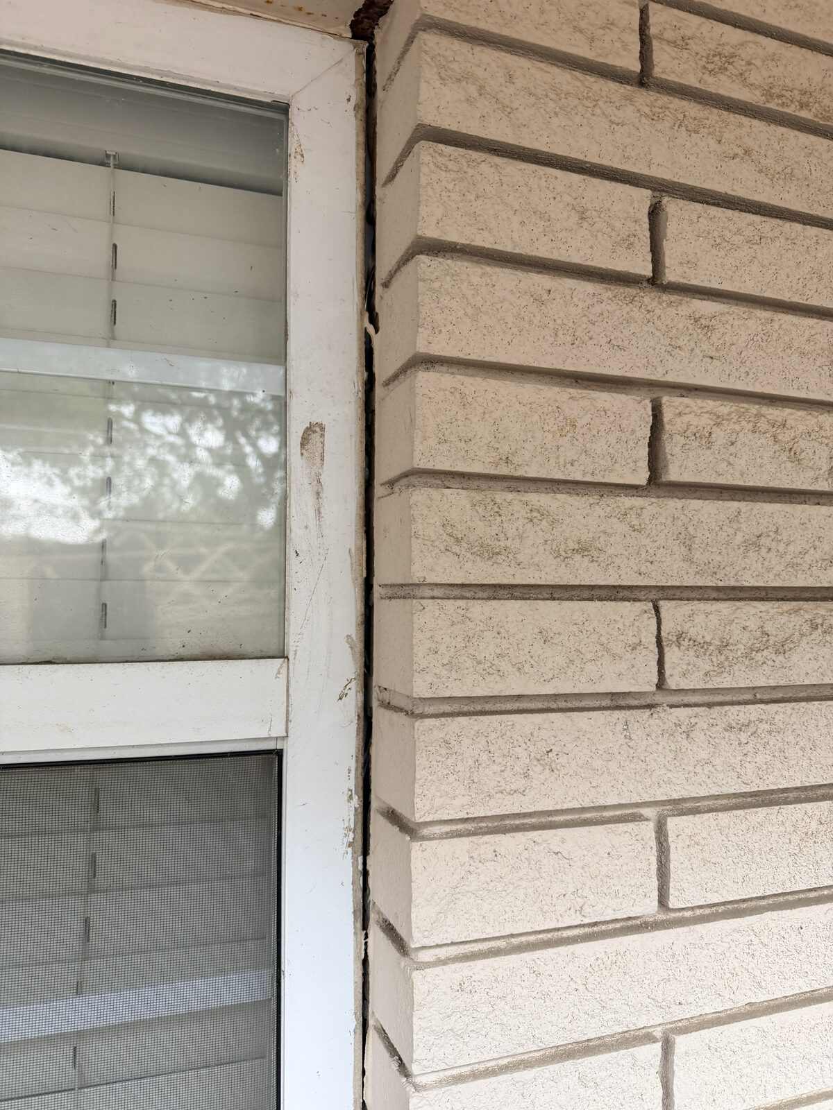 Vertical crack running along a window jamb through stone veneer, a sign of foundation settlement on a Hill Country home