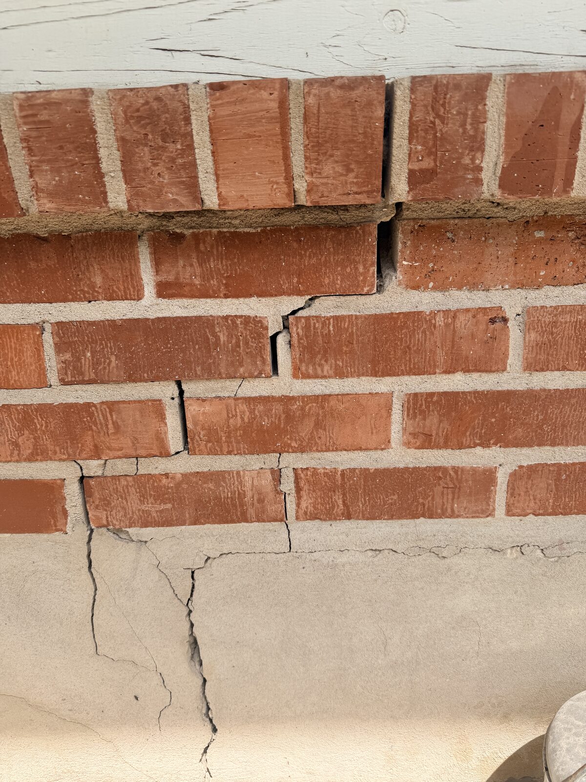 Crack in the exposed concrete grade beam below red brick veneer, evidence of foundation settlement
