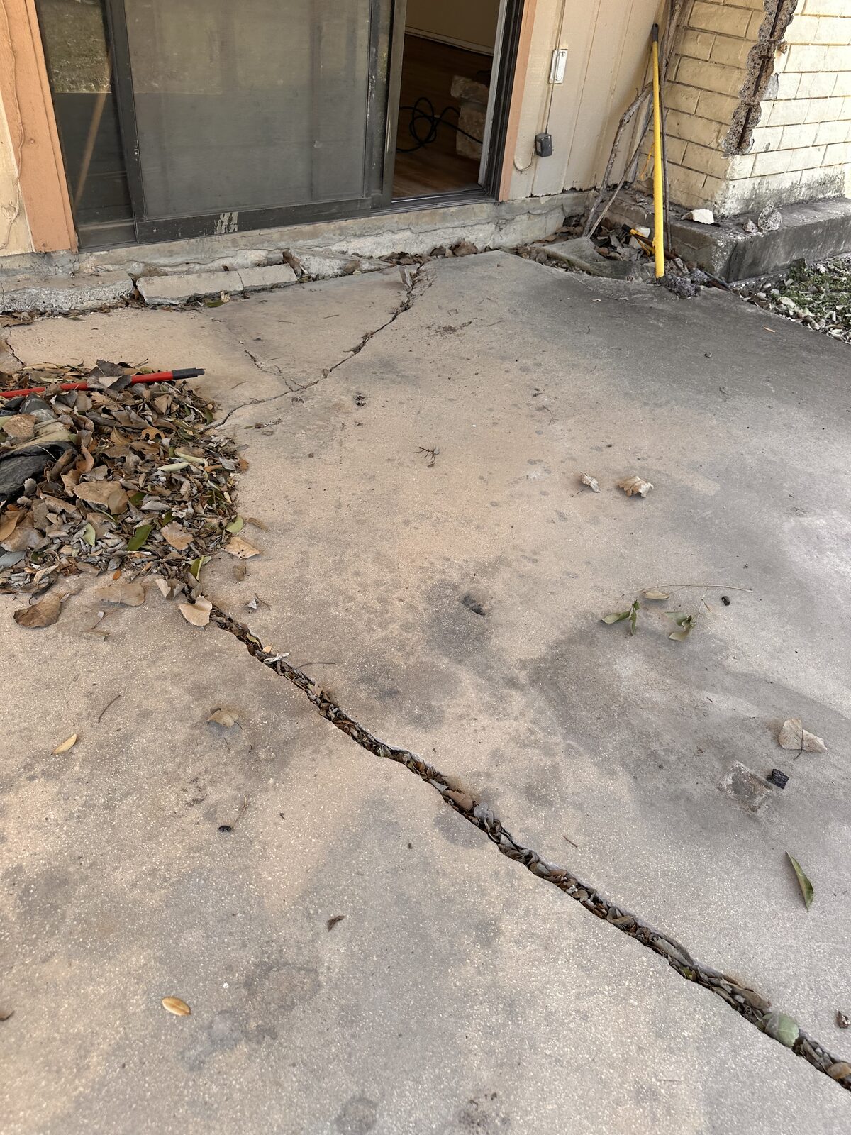 Settlement crack running across a concrete patio slab beside the lawn during a foundation inspection