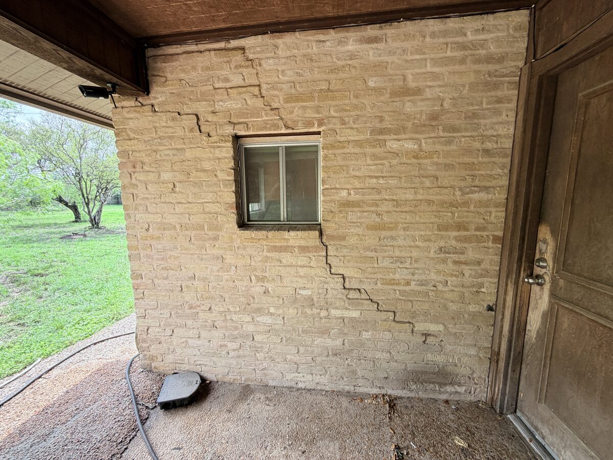 Wide view of a covered porch wall with a long diagonal stair-step crack from roofline to slab, before foundation repair