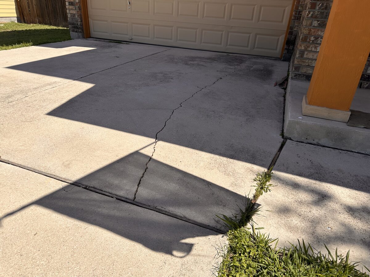 Cracked concrete patio slab at a covered porch corner, a sign of soil movement under the slab