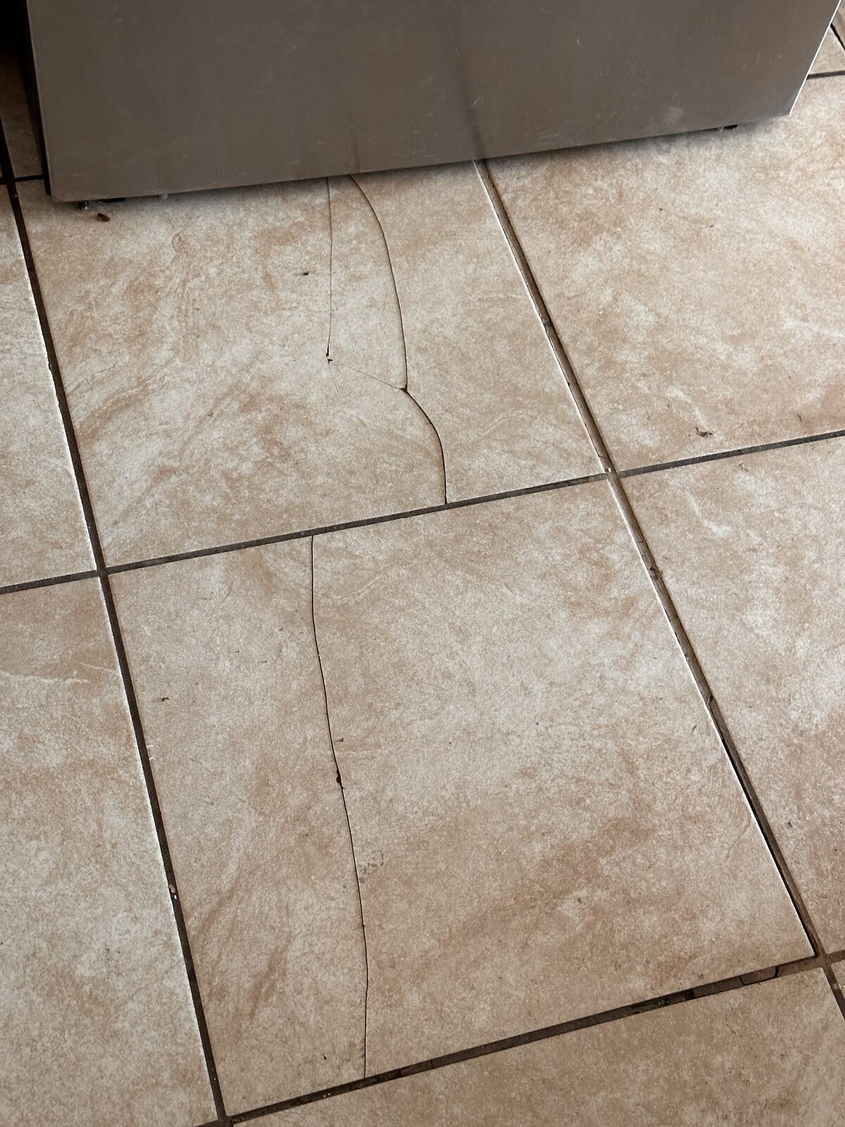 Cracked ceramic floor tiles beside an appliance, caused by movement in the slab foundation