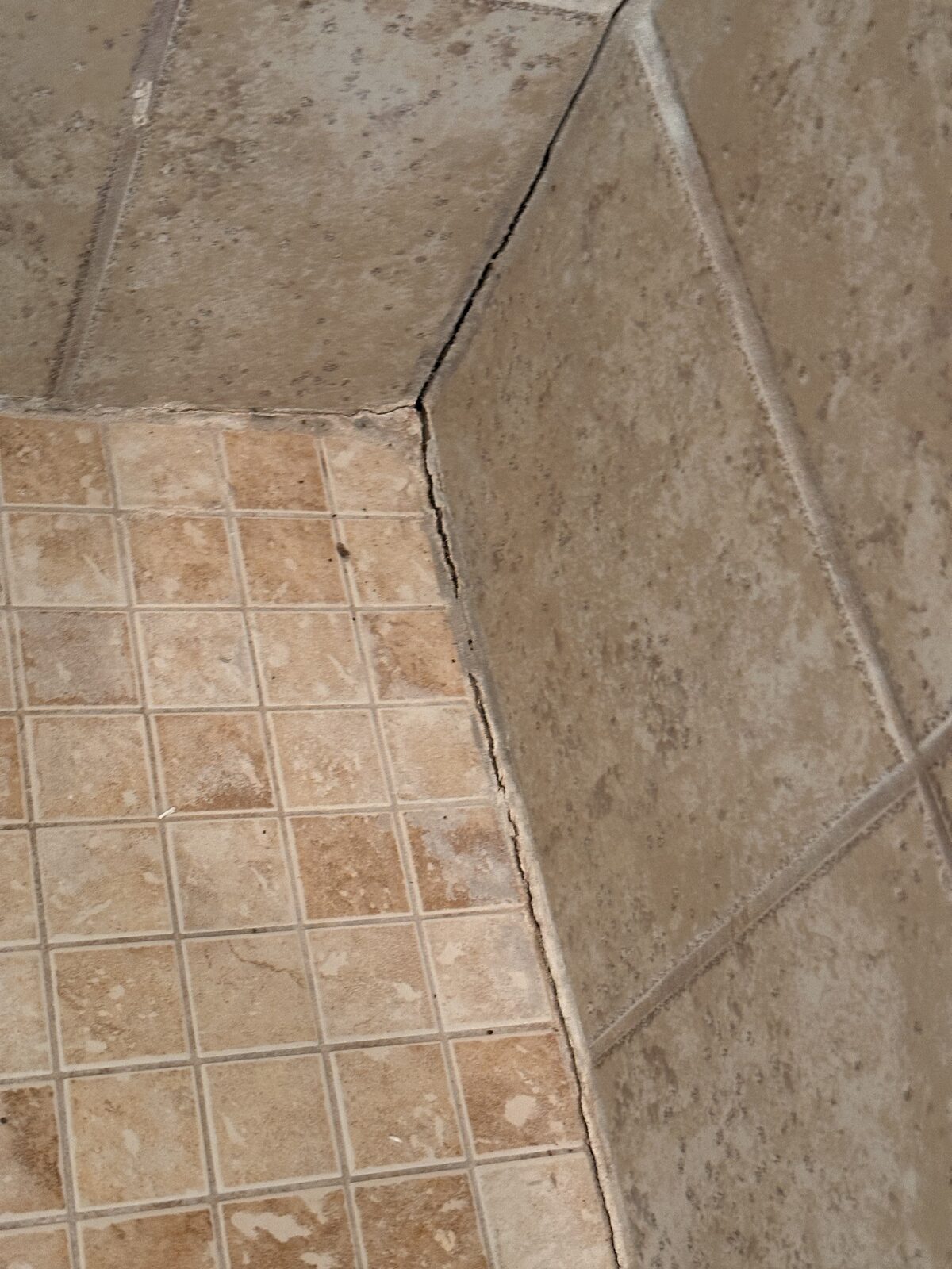 Cracked grout at a tiled shower corner with mosaic floor, an interior sign of foundation movement