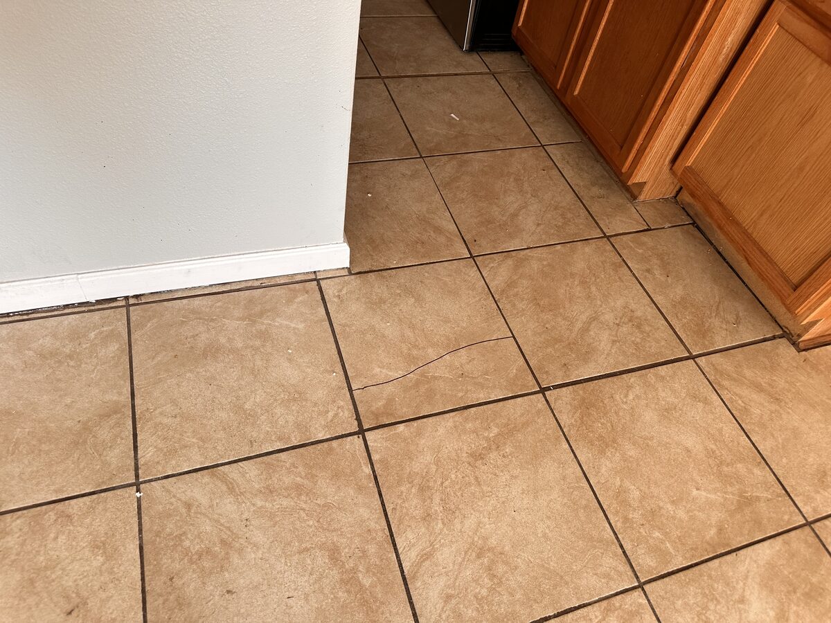 Cracked ceramic floor tile in a kitchen, often caused by slab foundation movement underneath