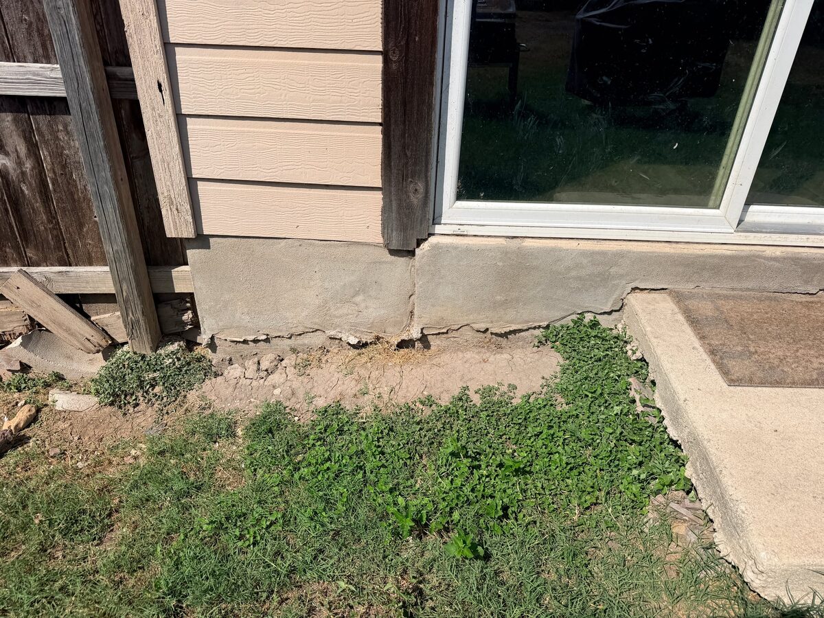 Exposed slab edge under a sliding patio door with a crack, chipped concrete and a gap in the soil