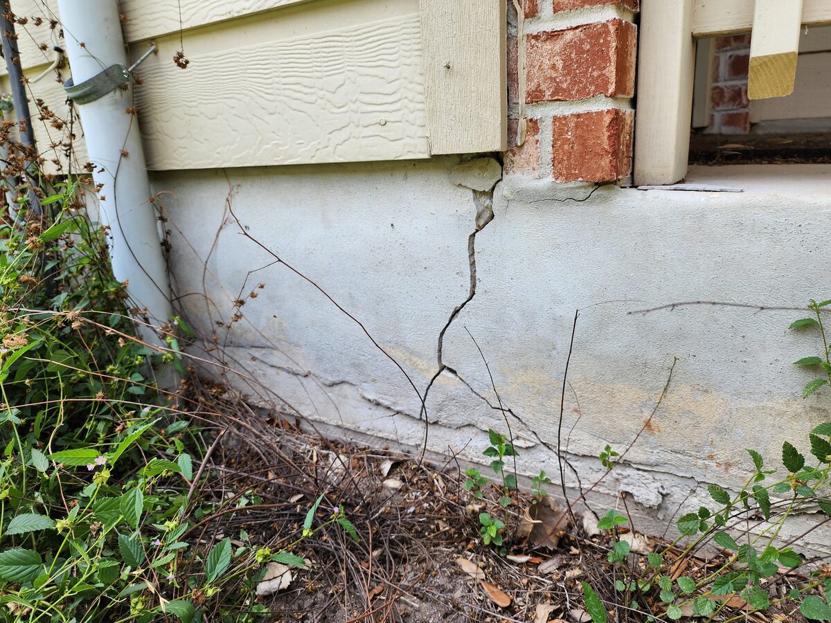 Cracked foundation stem wall at the corner of a brick-and-siding home, documented before foundation repair