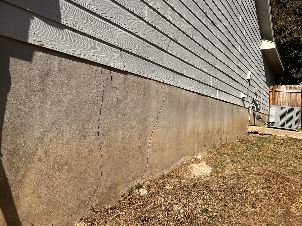 Cracked stem wall running along the side of a home near the A/C units, photographed during a foundation evaluation