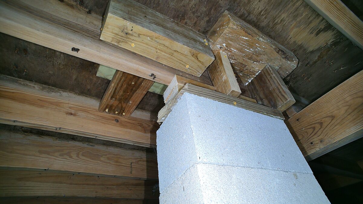 Concrete block pier with stacked wood shims under a floor beam, filmed by a crawler drone