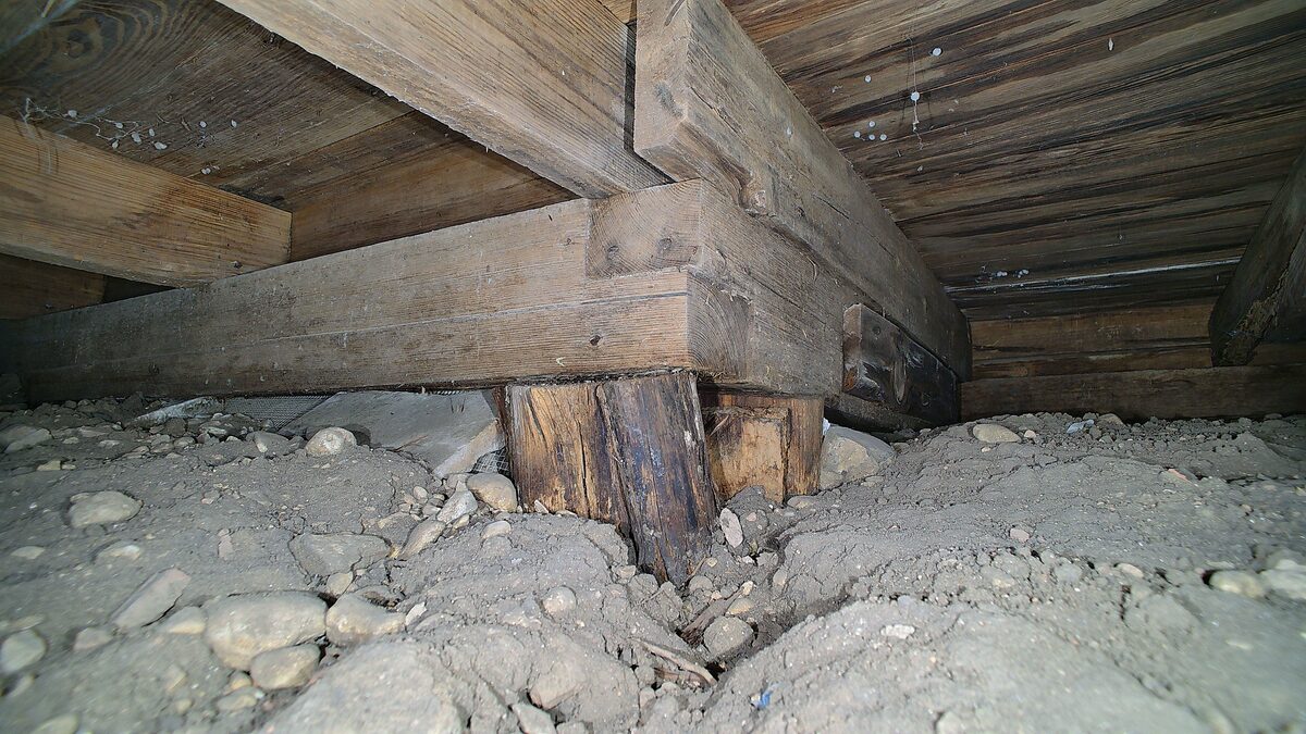 Old wood post under a floor beam on rocky clay soil in a crawl space