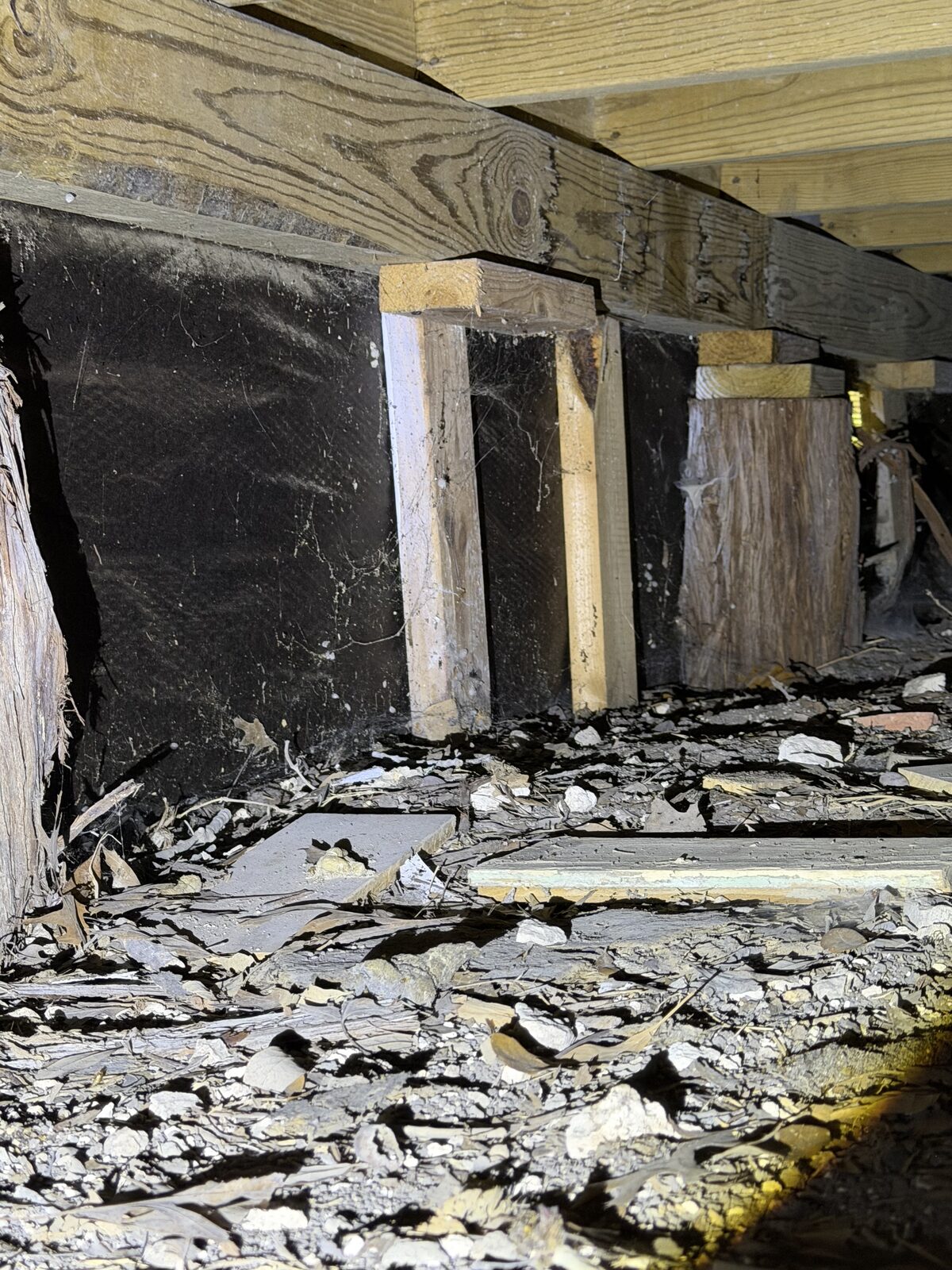 Crawlspace with wood joists, temporary cribbing, and a rubble stone perimeter wall