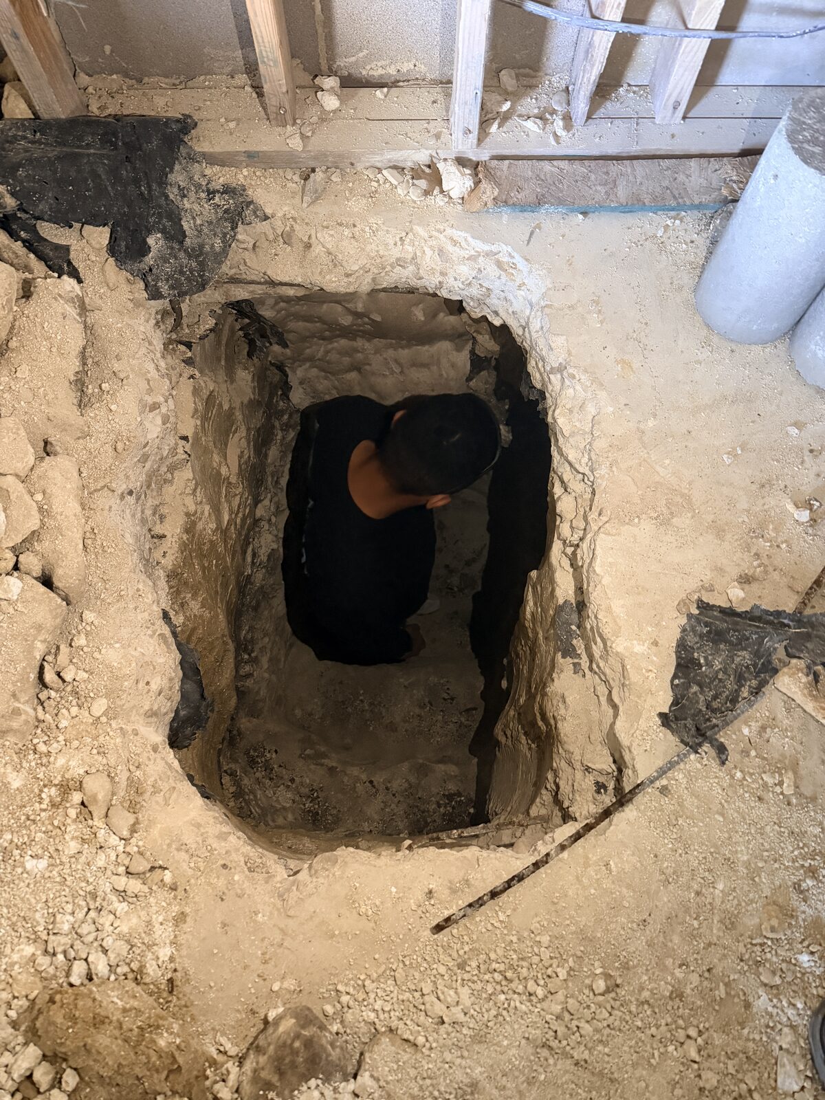 Crew hand-digging a deep pier pit below floor level during foundation repair