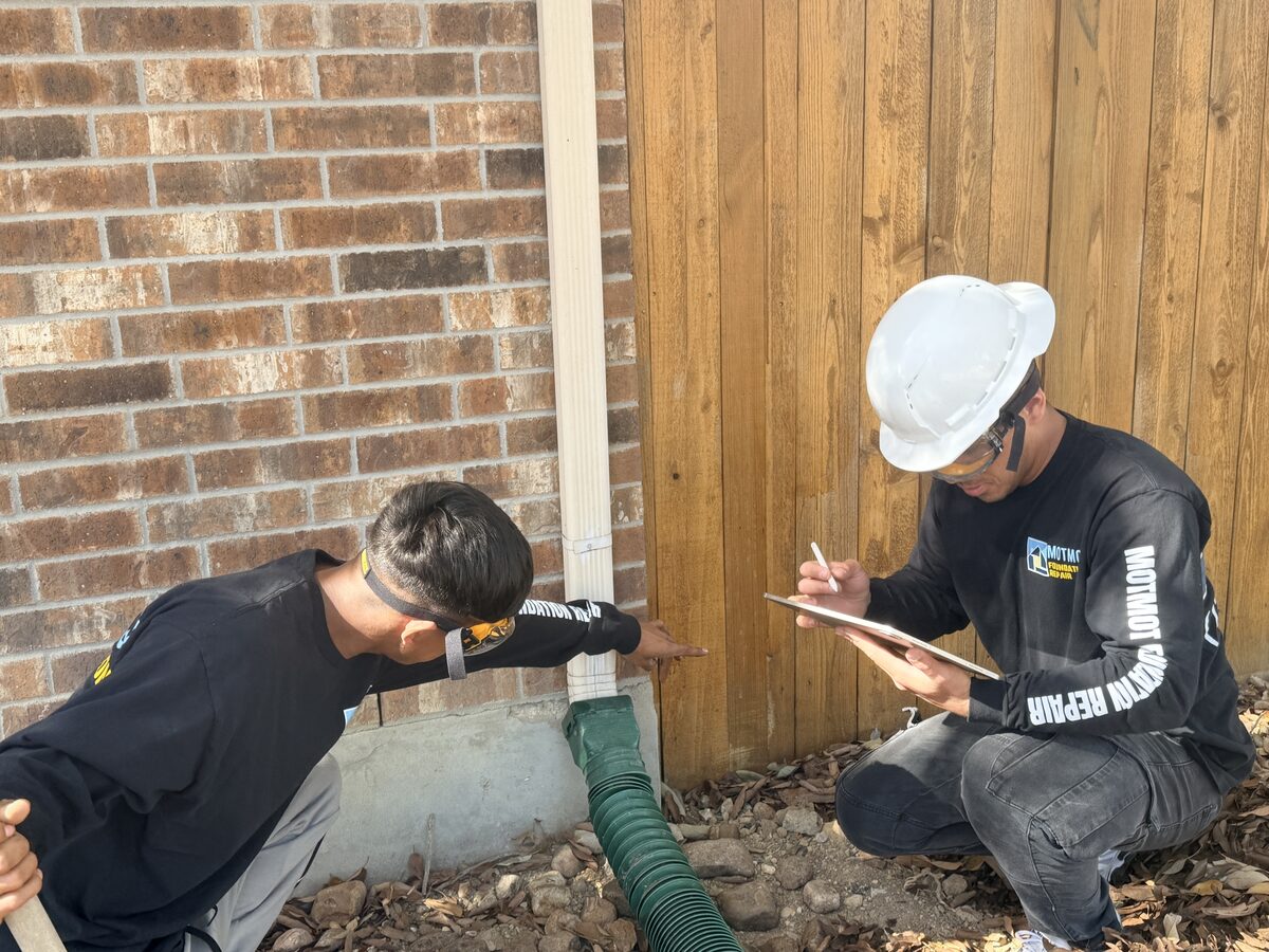 Motmot crew evaluating downspout drainage at the slab edge of a home