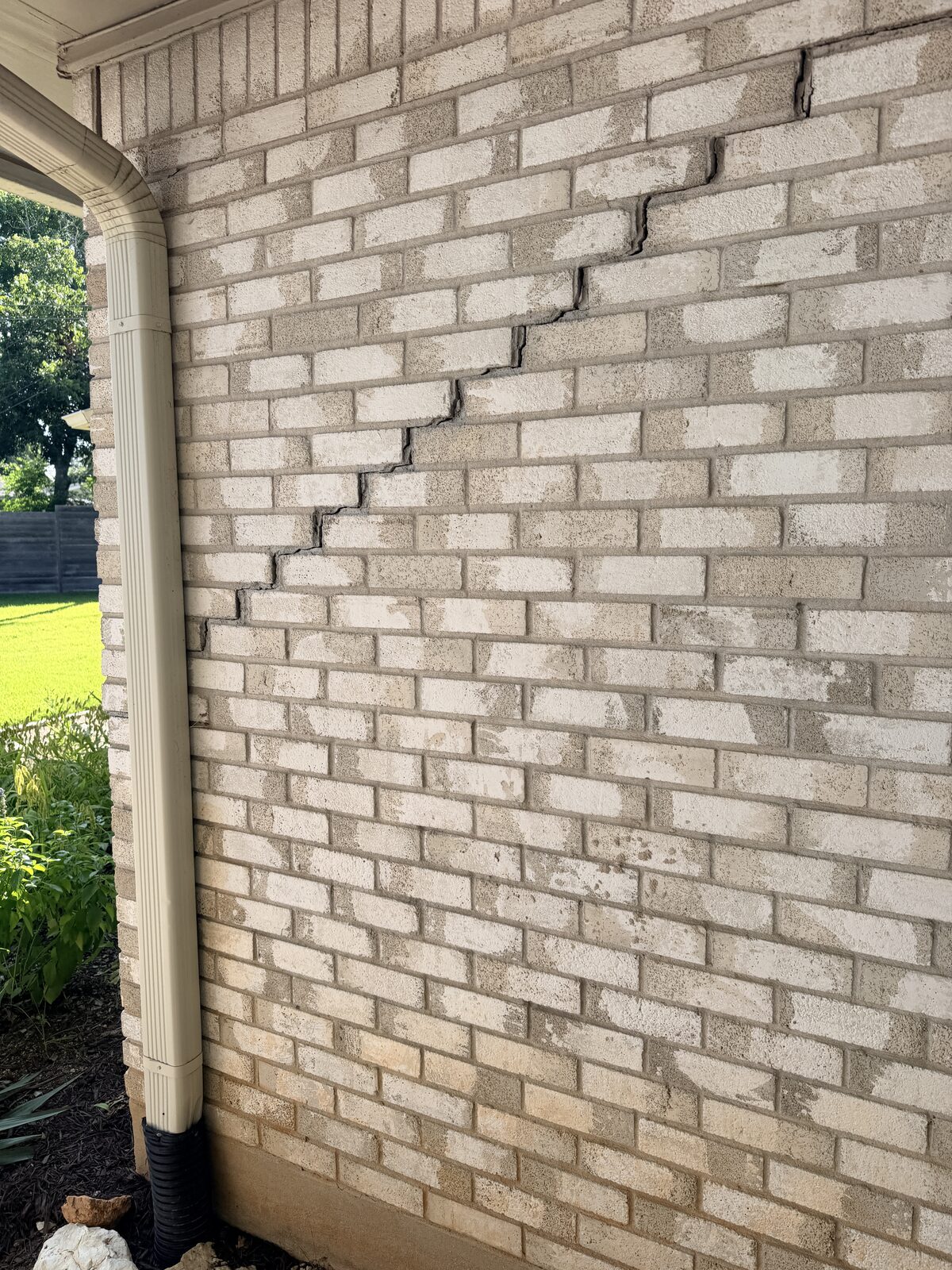 Diagonal stair step crack crossing brick veneer near a porch downspout