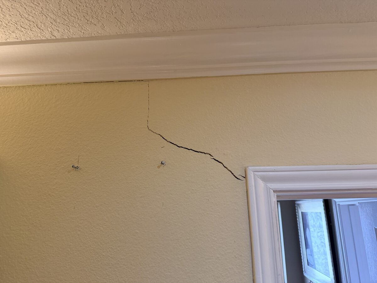Diagonal drywall crack reaching toward crown molding beside a mirror