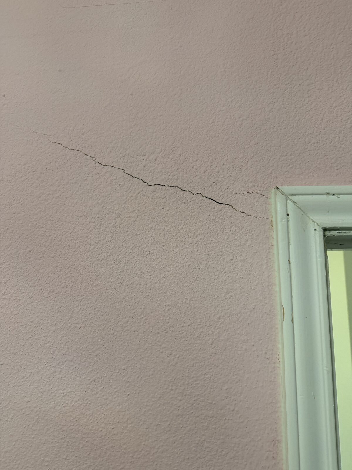 Diagonal drywall crack reaching a door frame corner, photographed during a foundation evaluation