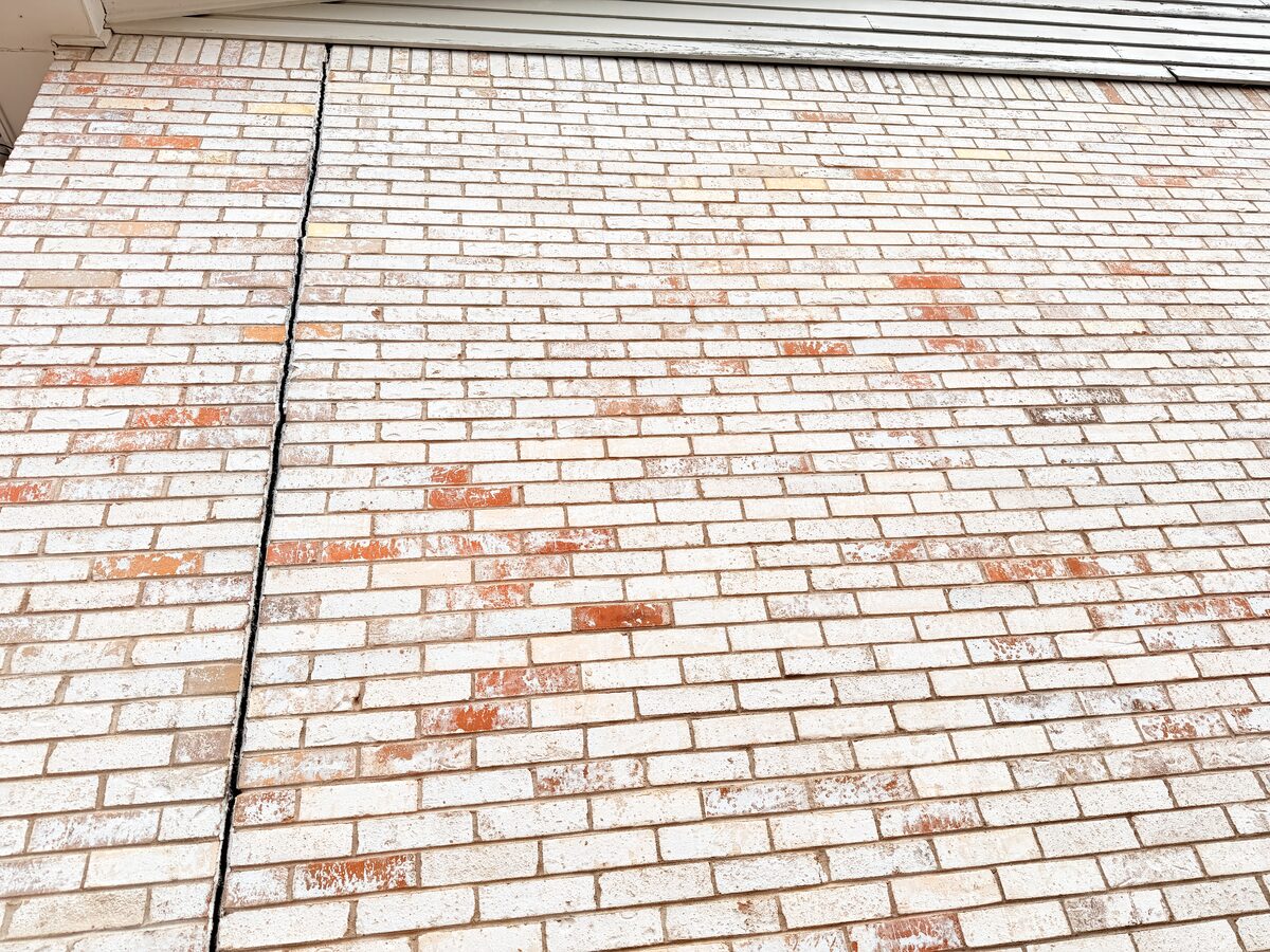 Diagonal repointed crack line descending a brick wall toward the walkway after foundation leveling