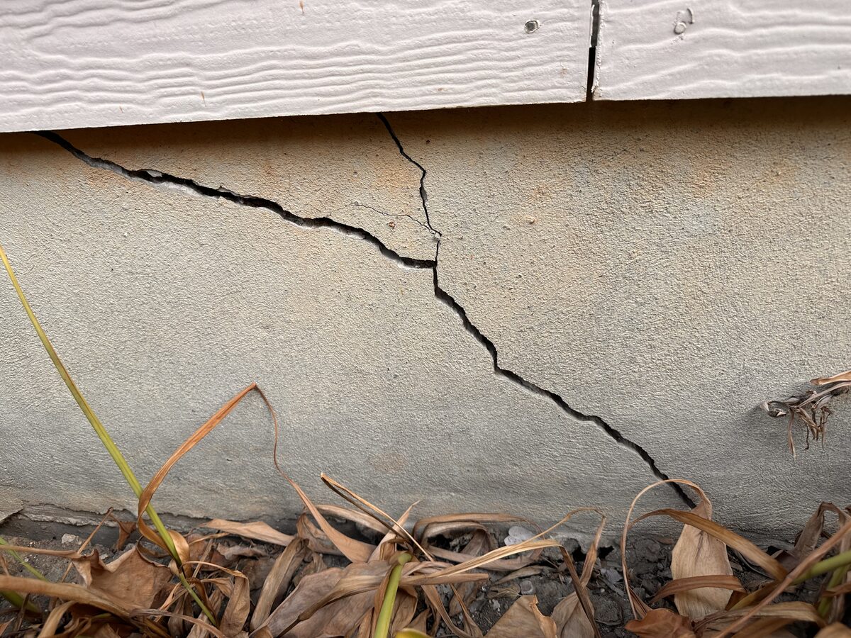Diagonal settlement crack in the parge-coated stem wall at a home's slab foundation