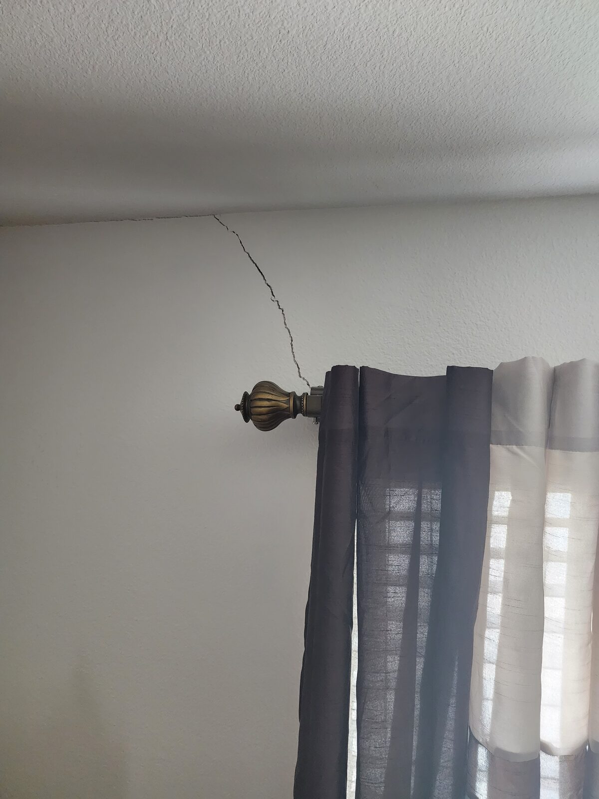 Diagonal drywall crack spreading from a bedroom window corner, a common interior sign of foundation settlement